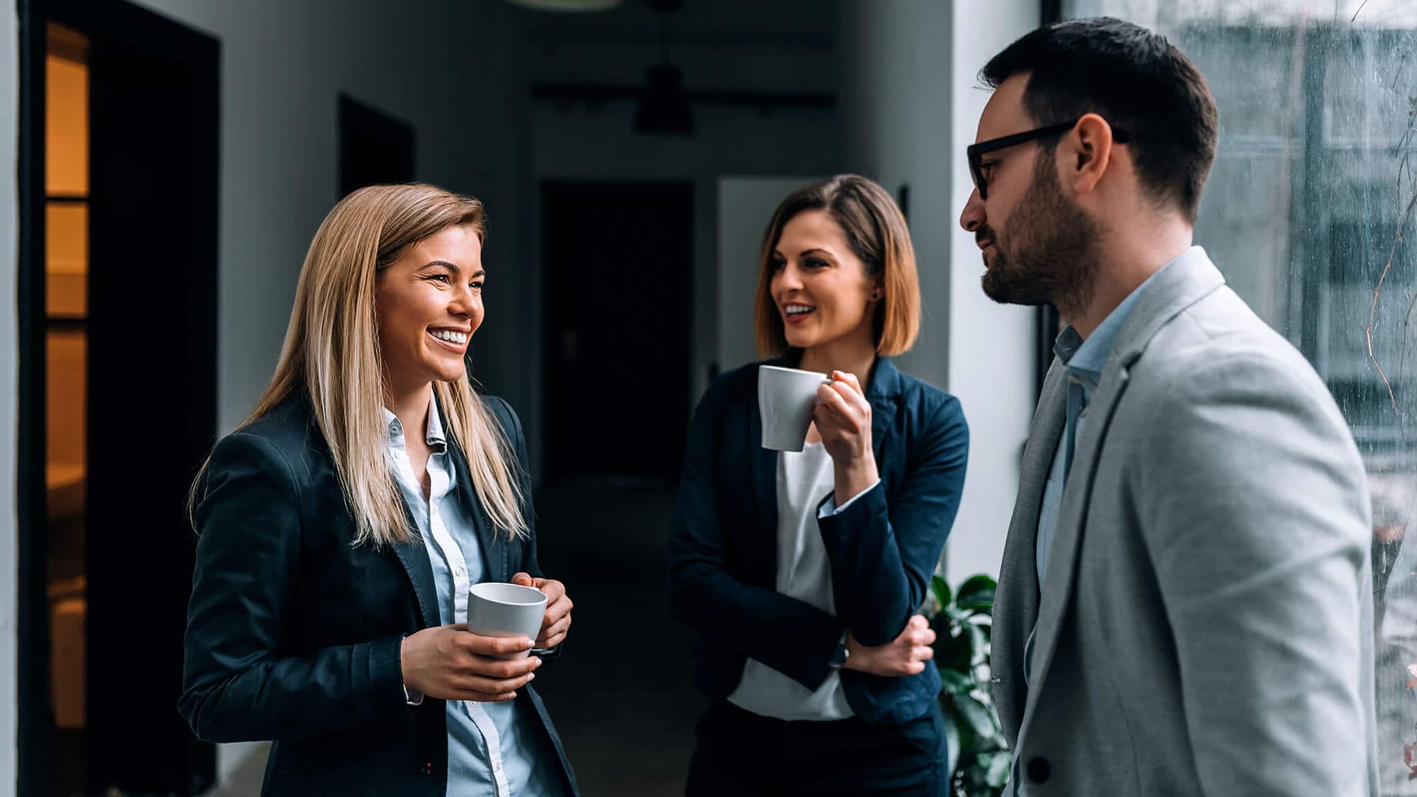 Two women and one man in conversation holding coffee