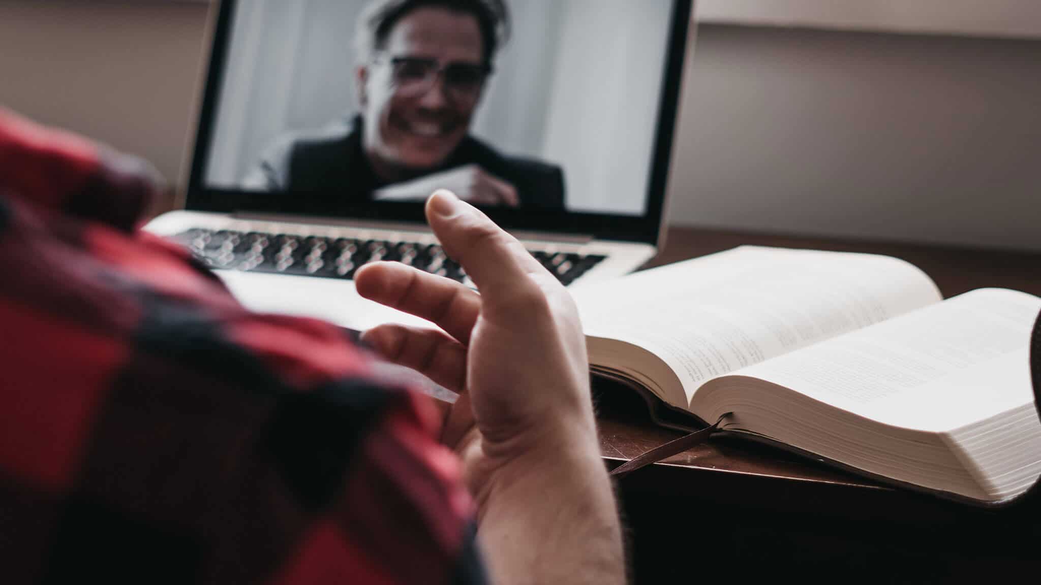 Over the shoulder shot of man&#039;s hand, open book, and laptop