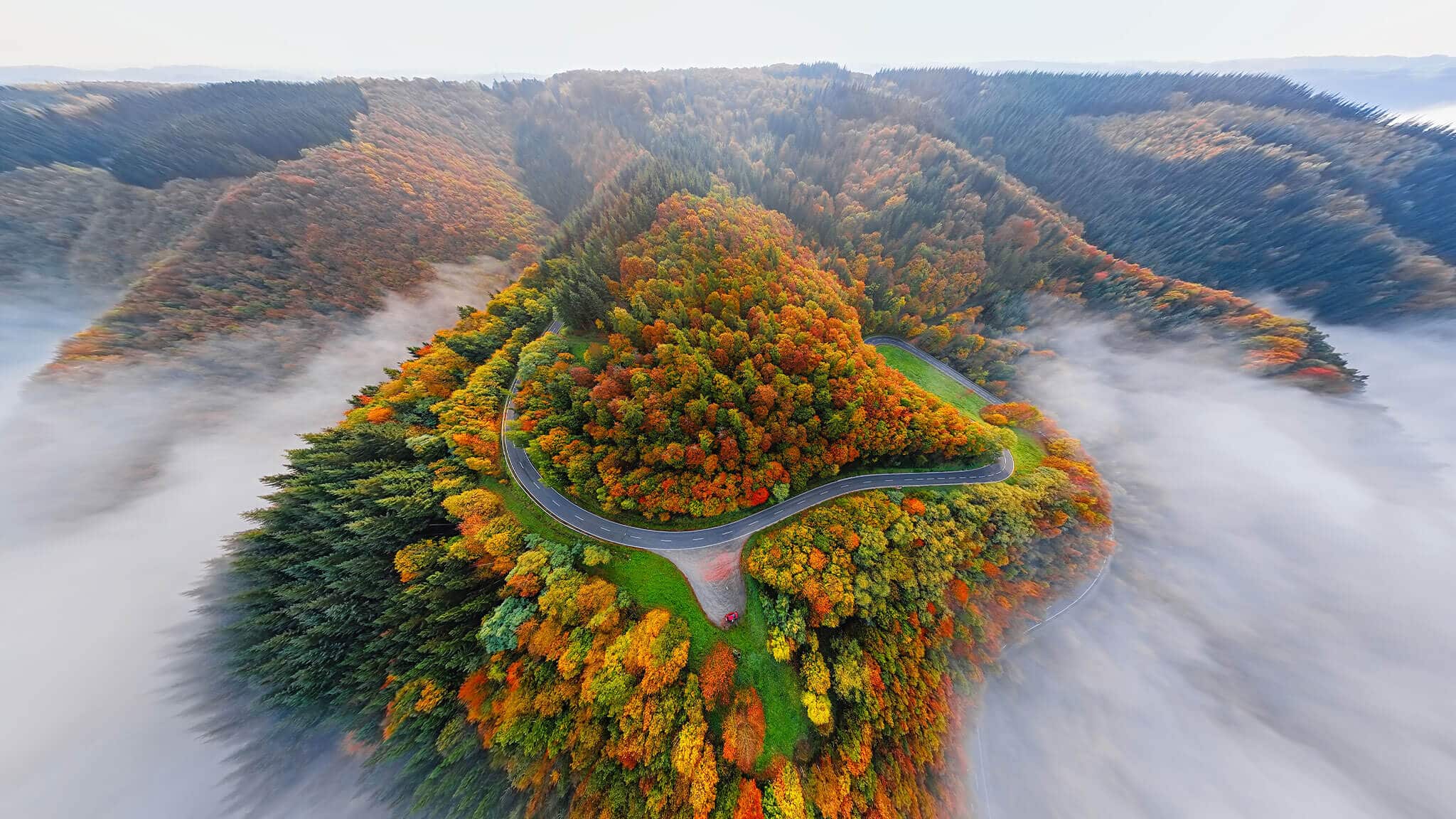 Aerial fish eye shot of tree covered hills and road in the mist