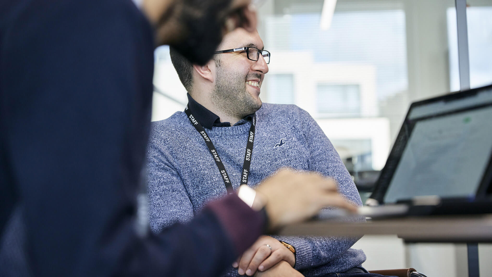 Over the shoulder view of man with light beard and glasses smiling looking to the right