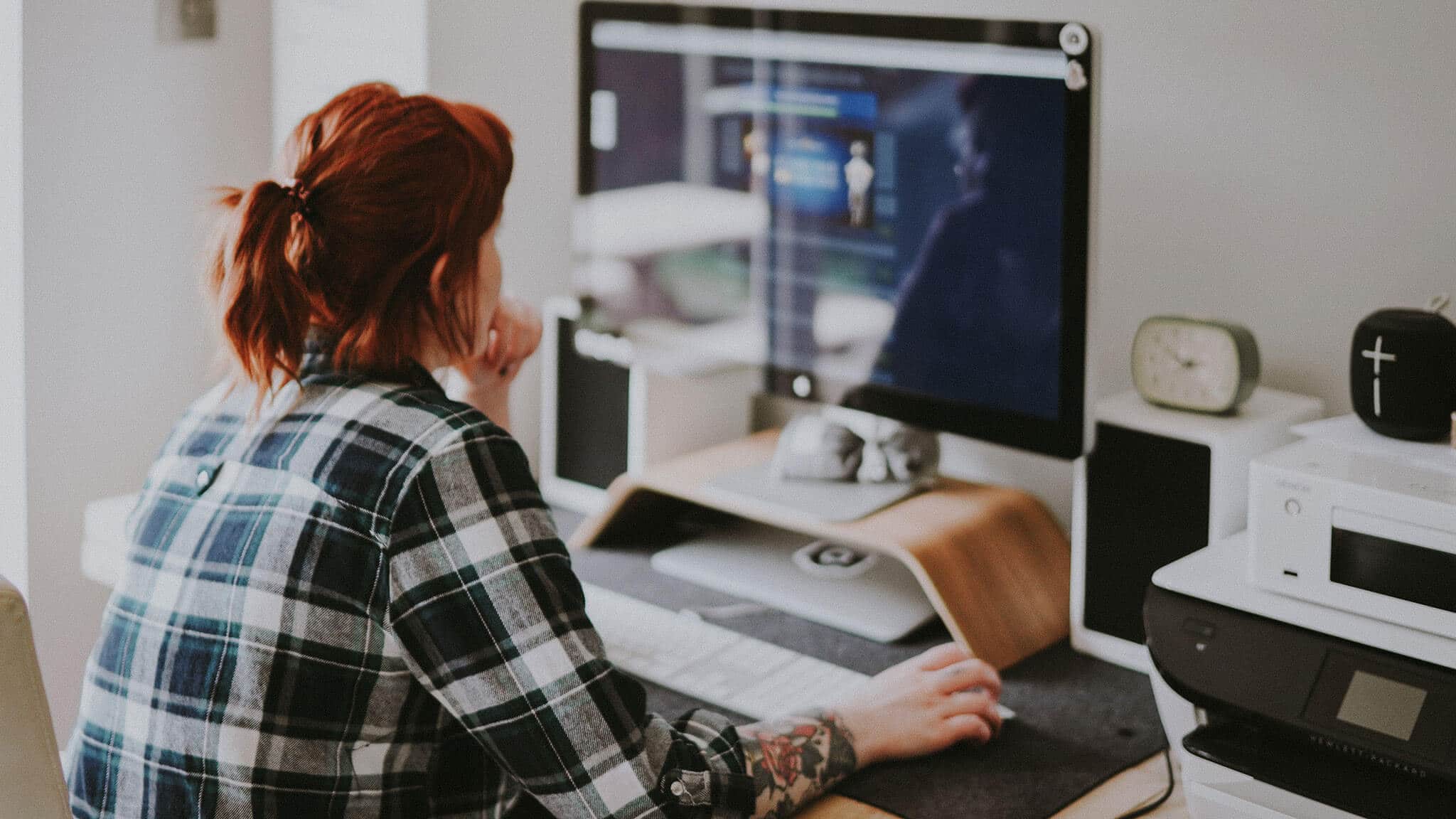 Redheaded woman in plaid shirt and arm tattoo working on desktop