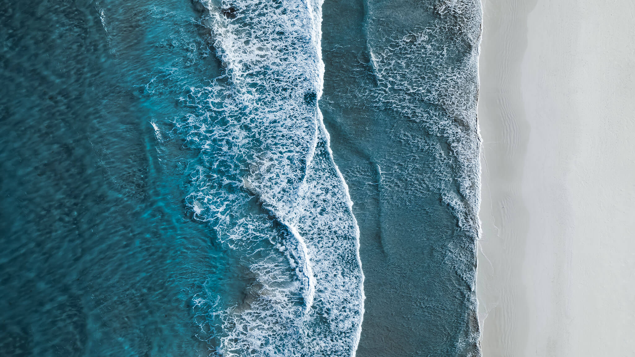 Aerial view of blue tide coming into a white sand beach