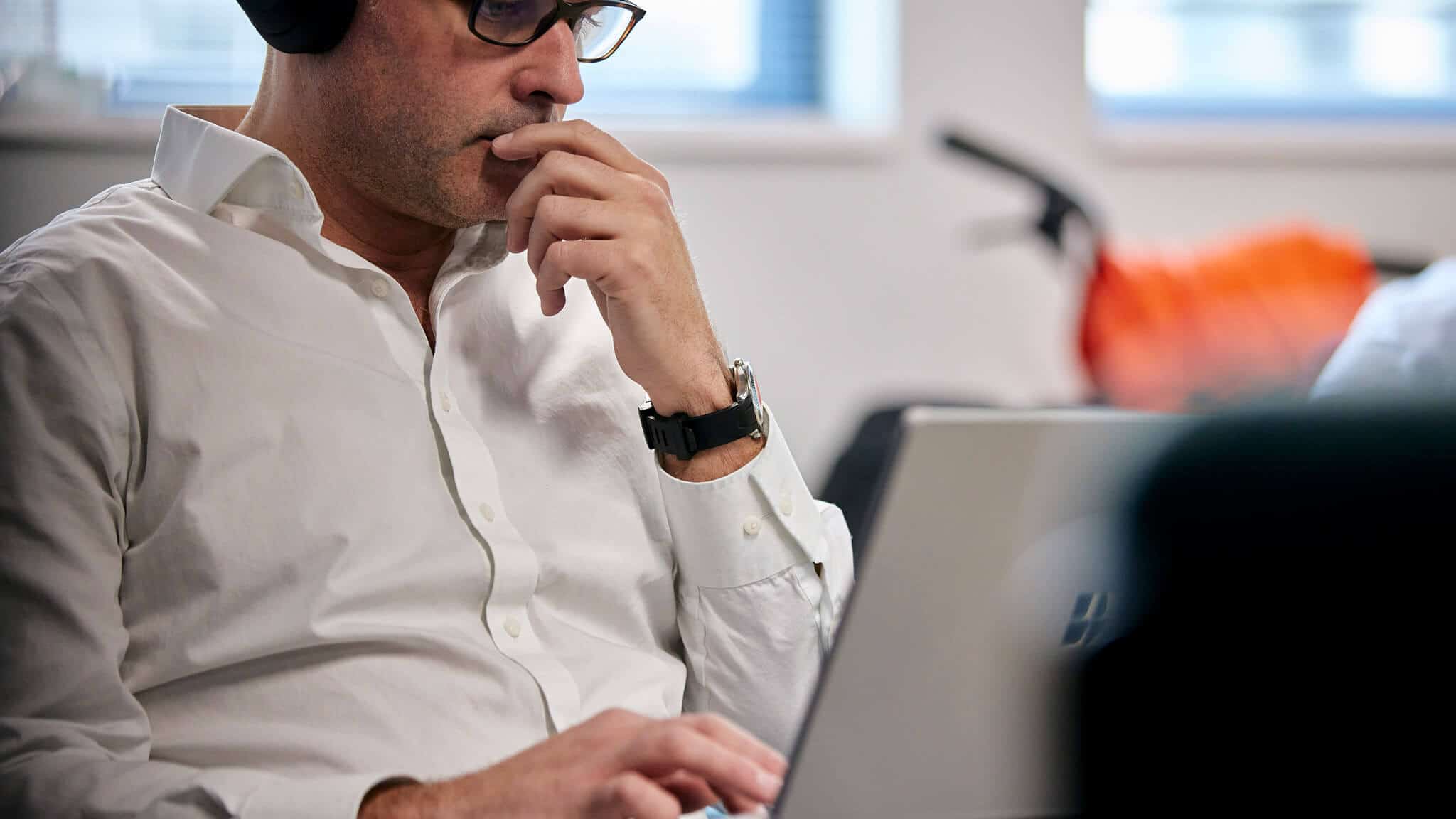 Closer shot of man in white shirt with glasses and headset staring at laptop screen