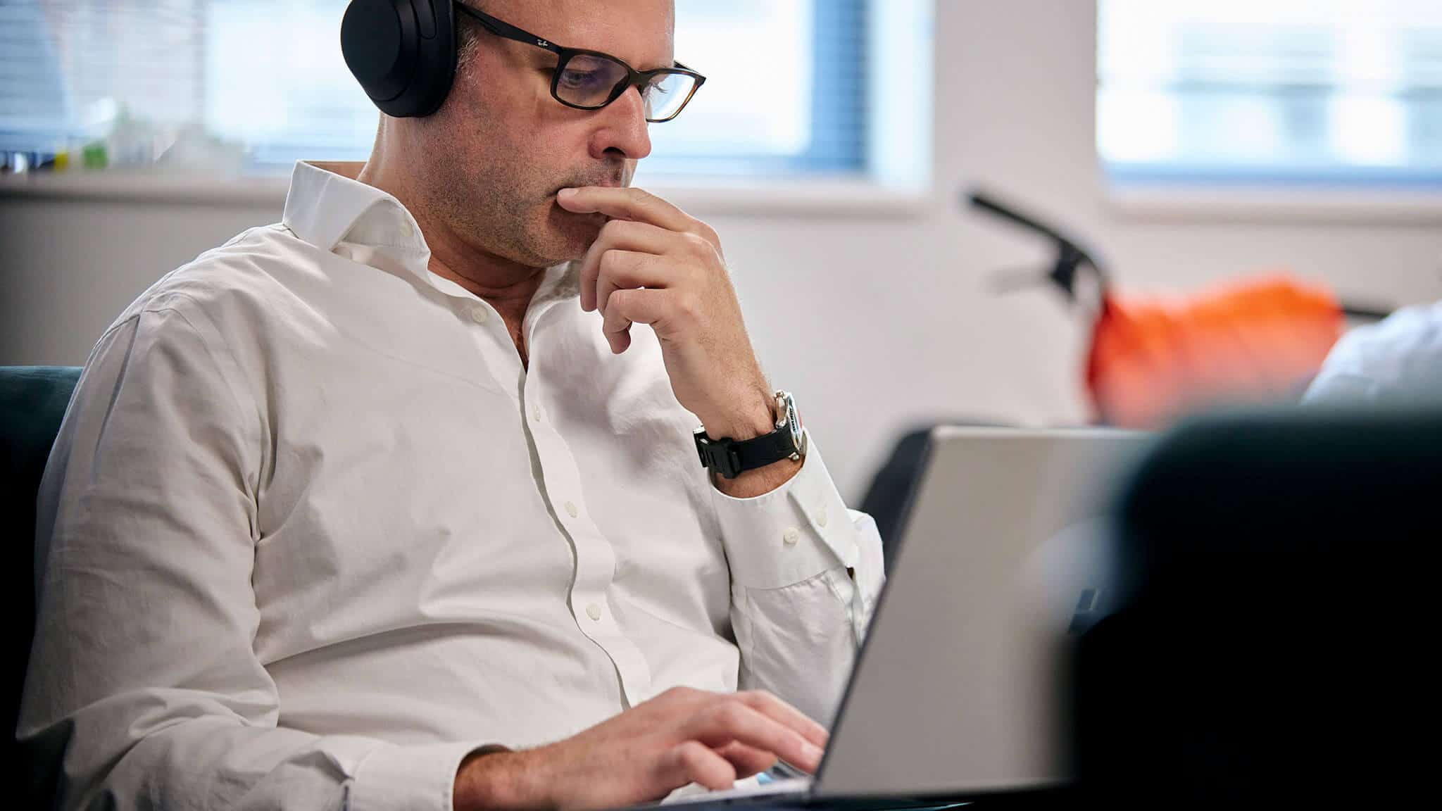 Man in white shirt with glasses and headset staring at laptop screen