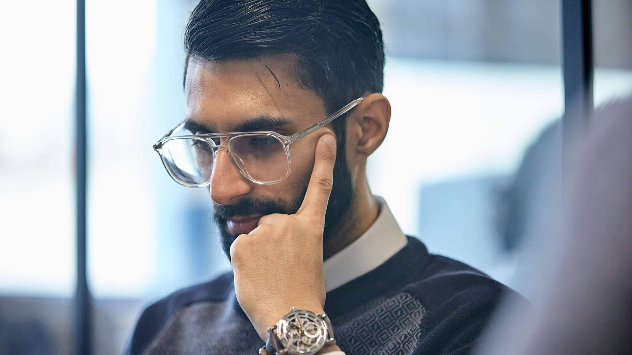 Man with dark hair, beard and glasses cradling face in concentration